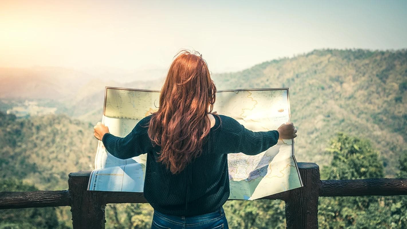 A woman holding a map in a balcony overlooking mountains and a forest